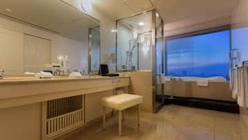 A modern bathroom with a large mirror, a vanity with toiletries, a bench, and a glass shower enclosure.