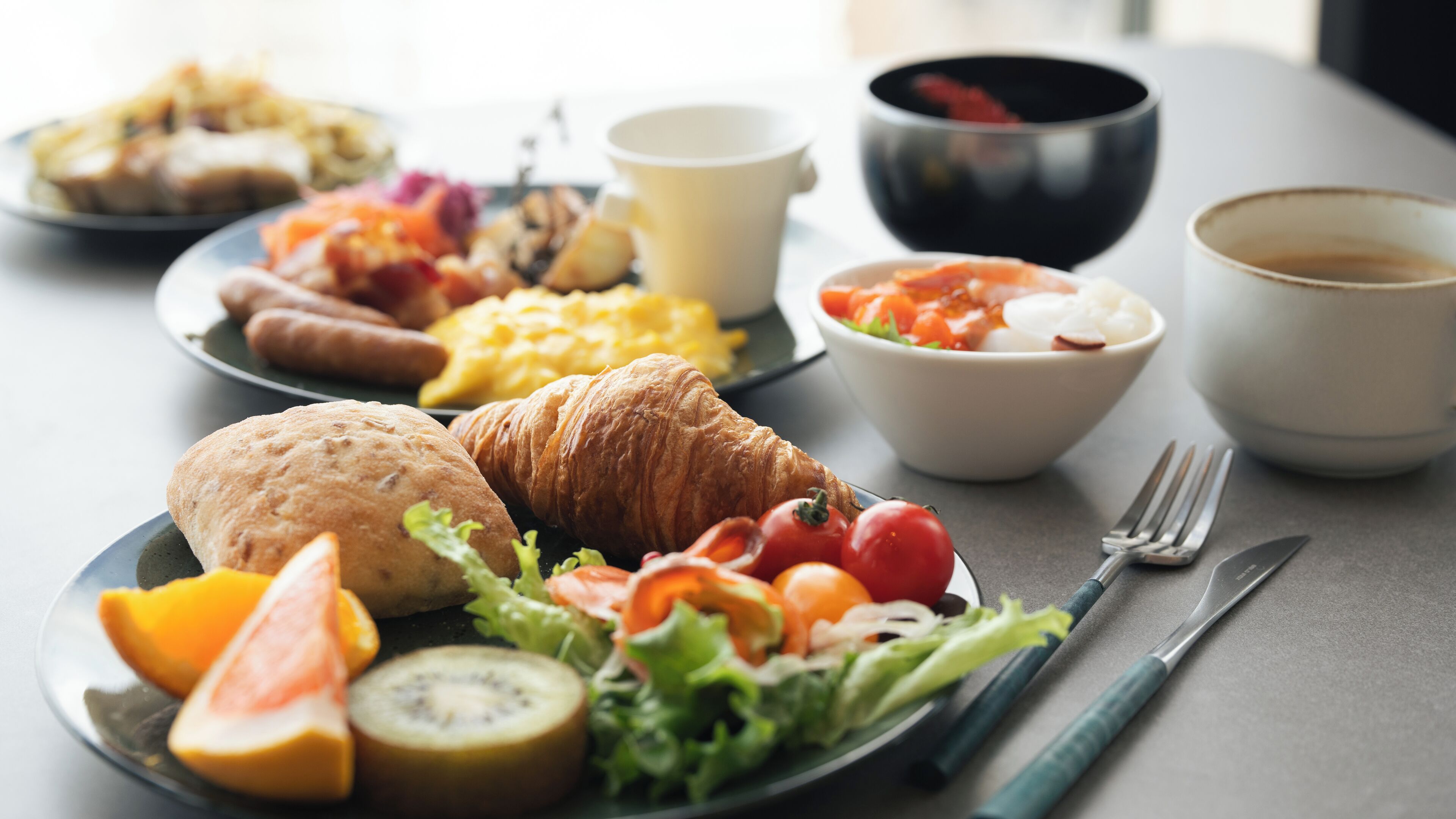 Una mesa con desayuno: cruasanes, frutas, verduras y café.