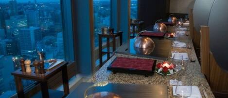 Un restaurante en un rascacielos con vistas panorámicas de la ciudad, decoración moderna y una larga mesa de comedor dispuesta para una comida.
