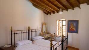 Ein Schlafzimmer mit Holzbalkendecke, einem Bett mit Metallkopfteil, einem Nachttisch, einem Stuhl, einem Schreibtisch, einem Spiegel und einem Fenster mit Blick.