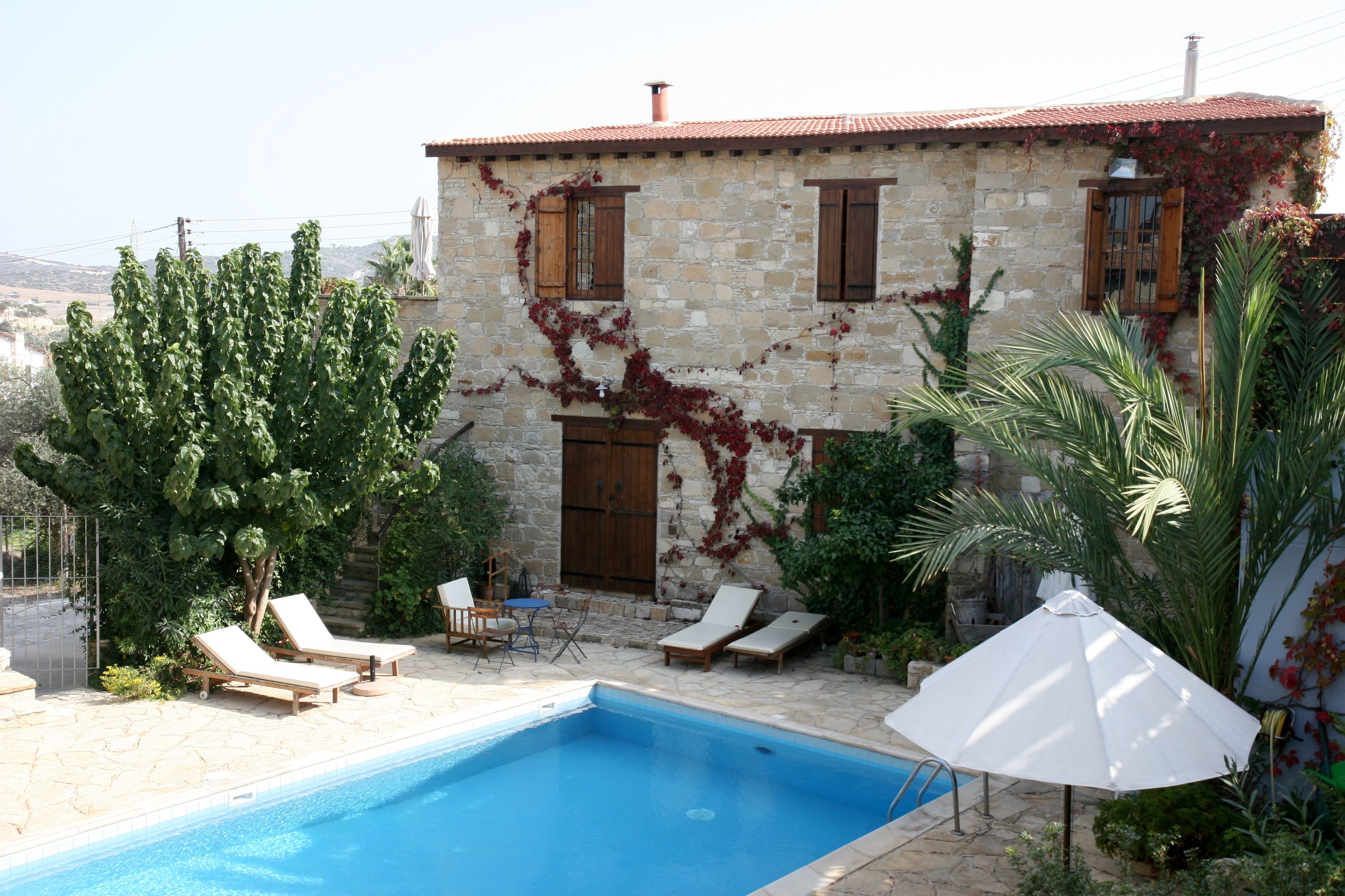 A stone house with a swimming pool, outdoor seating, and lush greenery.