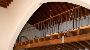 Ein geräumiger Wohnbereich mit hoher Holzbalkendecke, einer Treppe, einem Esstisch mit Stühlen und einem blauen, gepolsterten Sessel.