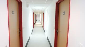 Ein langer, schmaler Hotelkorridor mit rot gerahmten Türen an beiden Seiten, weißen Wänden und einem weißen Teppich.