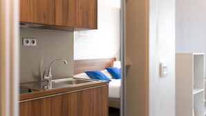 A compact kitchenette with wooden cabinets, a stainless steel sink, and a small countertop. - Appart'Hotel Victoria Garden Pau (Pau)