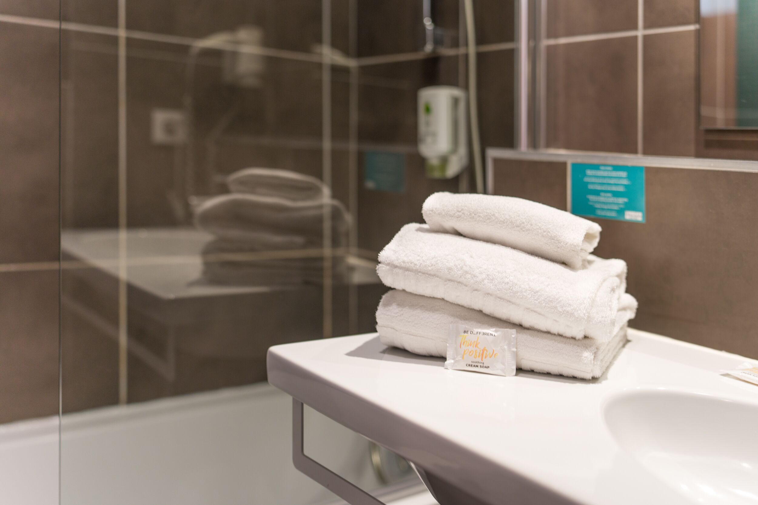 A bathroom with a stack of white towels on a counter, a soap dispenser, and a sign with text.