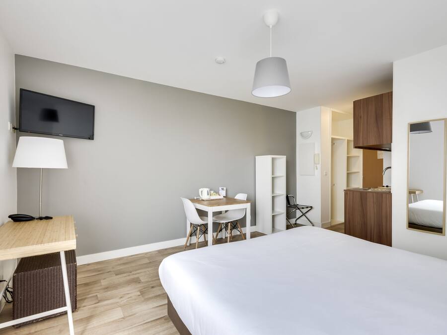 A modern hotel room with a large bed, a desk with a chair, a television mounted on the wall, and a wardrobe.