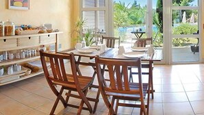 Un comedor con sillas de madera y una mesa, un mostrador de buffet con alimentos, y vistas a la vegetación a través de grandes ventanales.