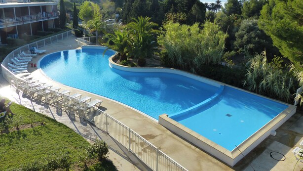 Una gran piscina curvada rodeada de sillones de descanso y una terraza, con vistas a una colina y árboles al fondo.