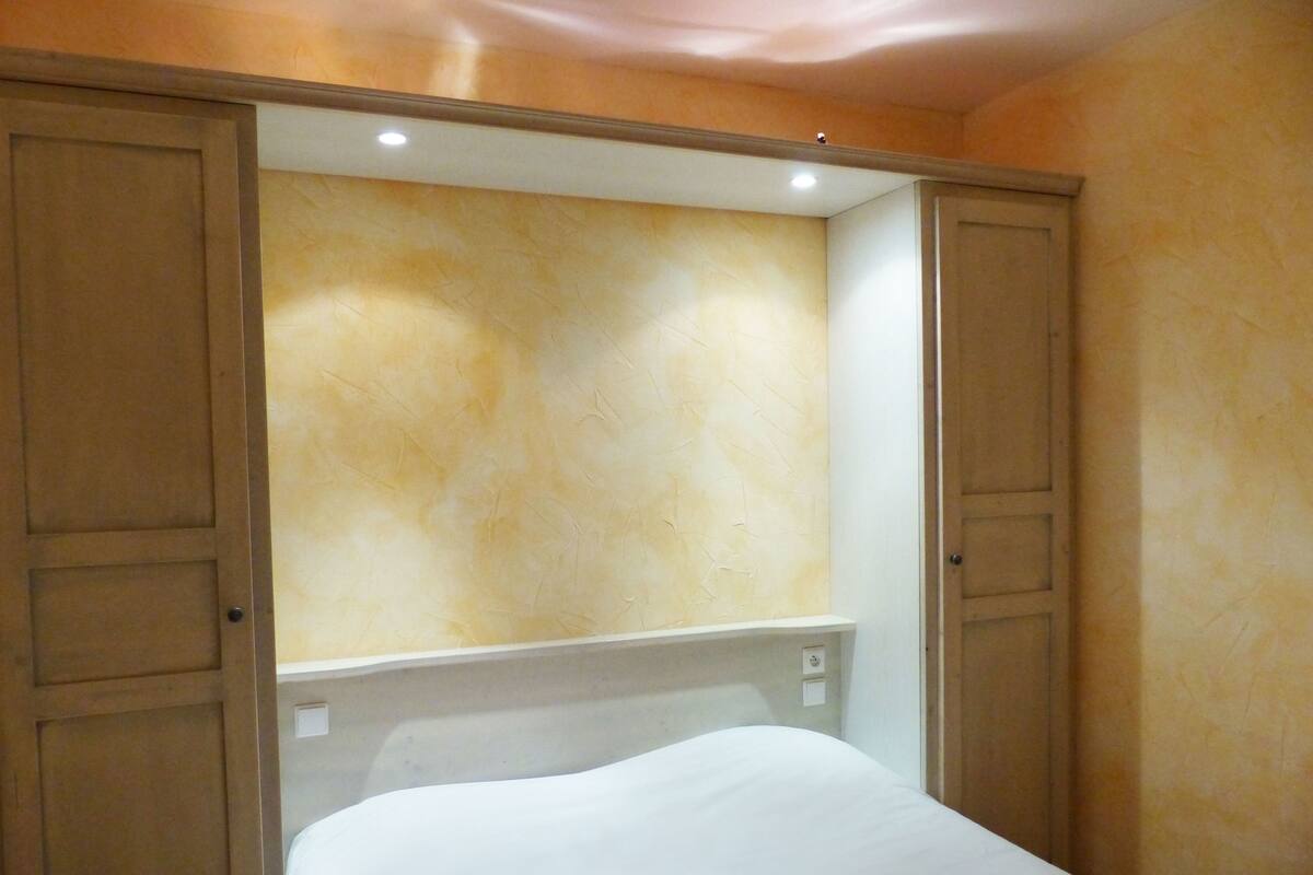 Una habitación pequeña con cama individual, un armario de madera y una pared lisa.