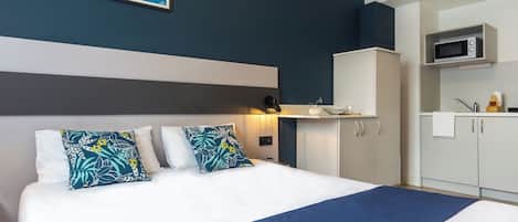 A hotel room with a bed, a nightstand, a microwave, and a small kitchenette.