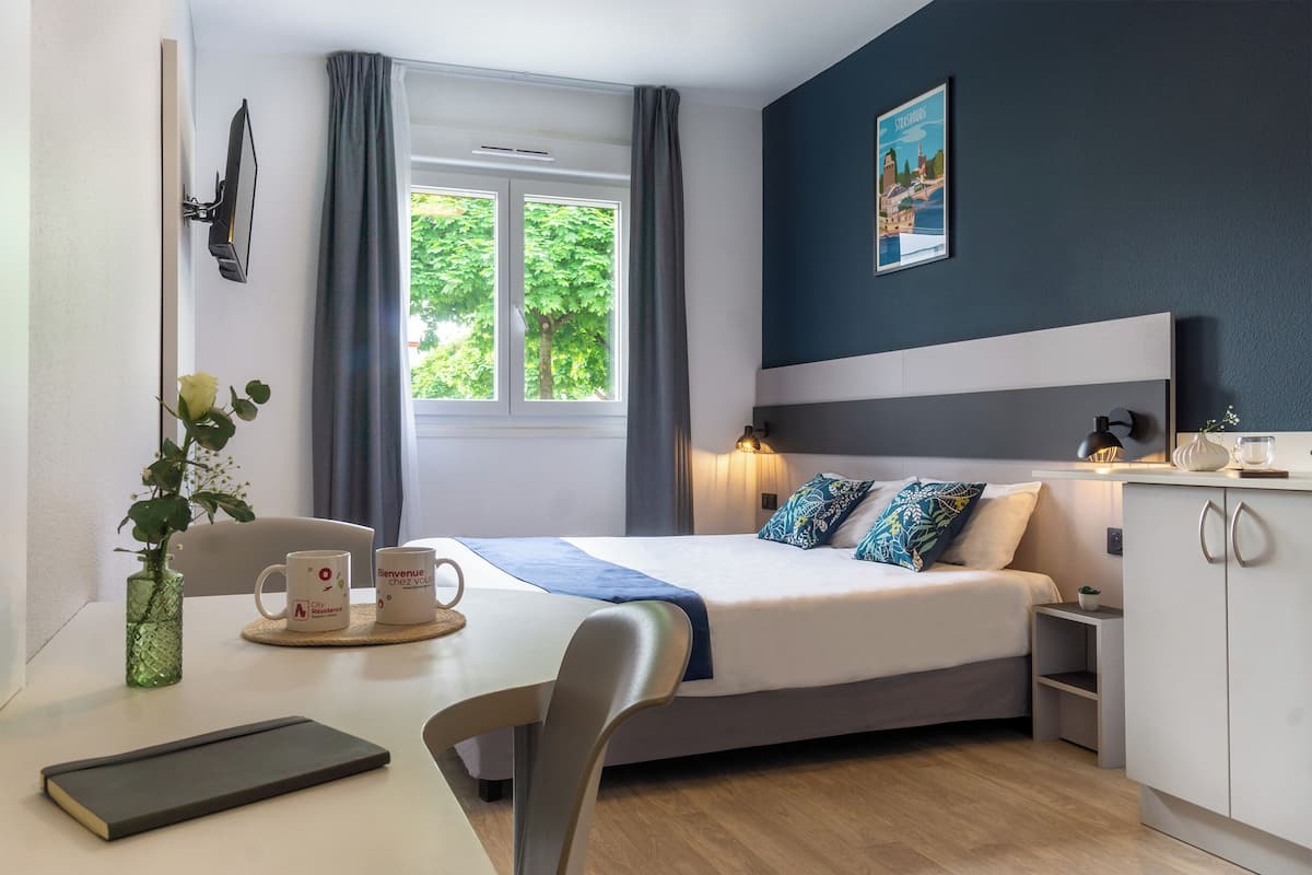A neatly arranged hotel room with a bed, bedside table, and a window with curtains.