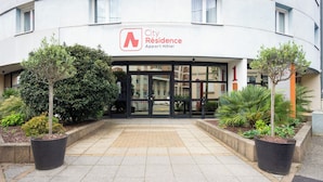 A building with a sign reading "City Residence Apartment Hotel." There are two potted plants on either side of the entrance.