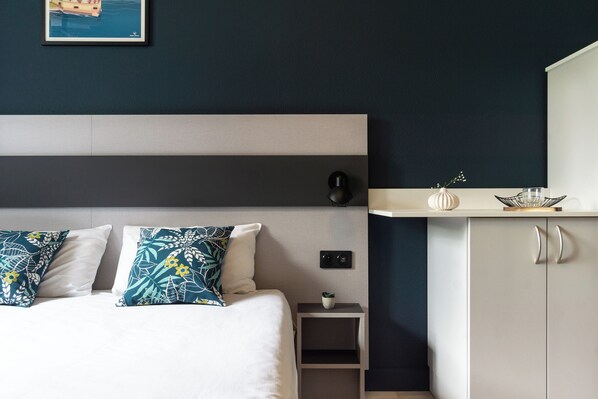 A modern bedroom with a bed, pillows, bedside table, nightstand, and a cabinet.