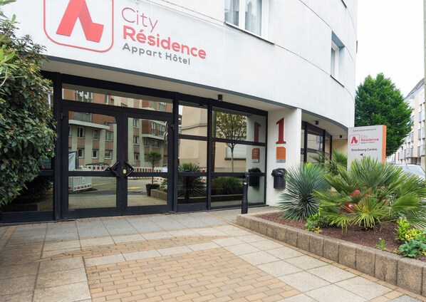 The exterior of City Residence, an apartment hotel with a modern design, featuring large glass doors and a well-maintained entrance area.