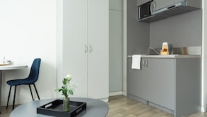 A modern kitchen with grey cabinets, a microwave, and a sink. There is a blue chair and a small table with a tray and a plant.