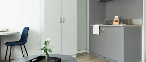 A modern kitchen with grey cabinets, a microwave, and a sink. There is a blue chair and a small table with a tray and a plant.