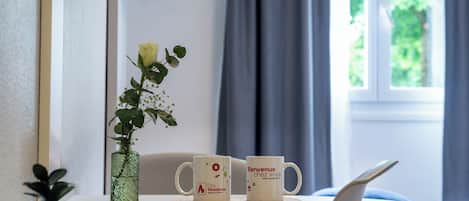 Una habitación de hotel con una cama, una mesita con dos tazas, un libro y una planta en maceta.