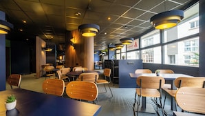 A modern restaurant interior with wooden tables and chairs, pendant lighting, and large windows offering views of the city.