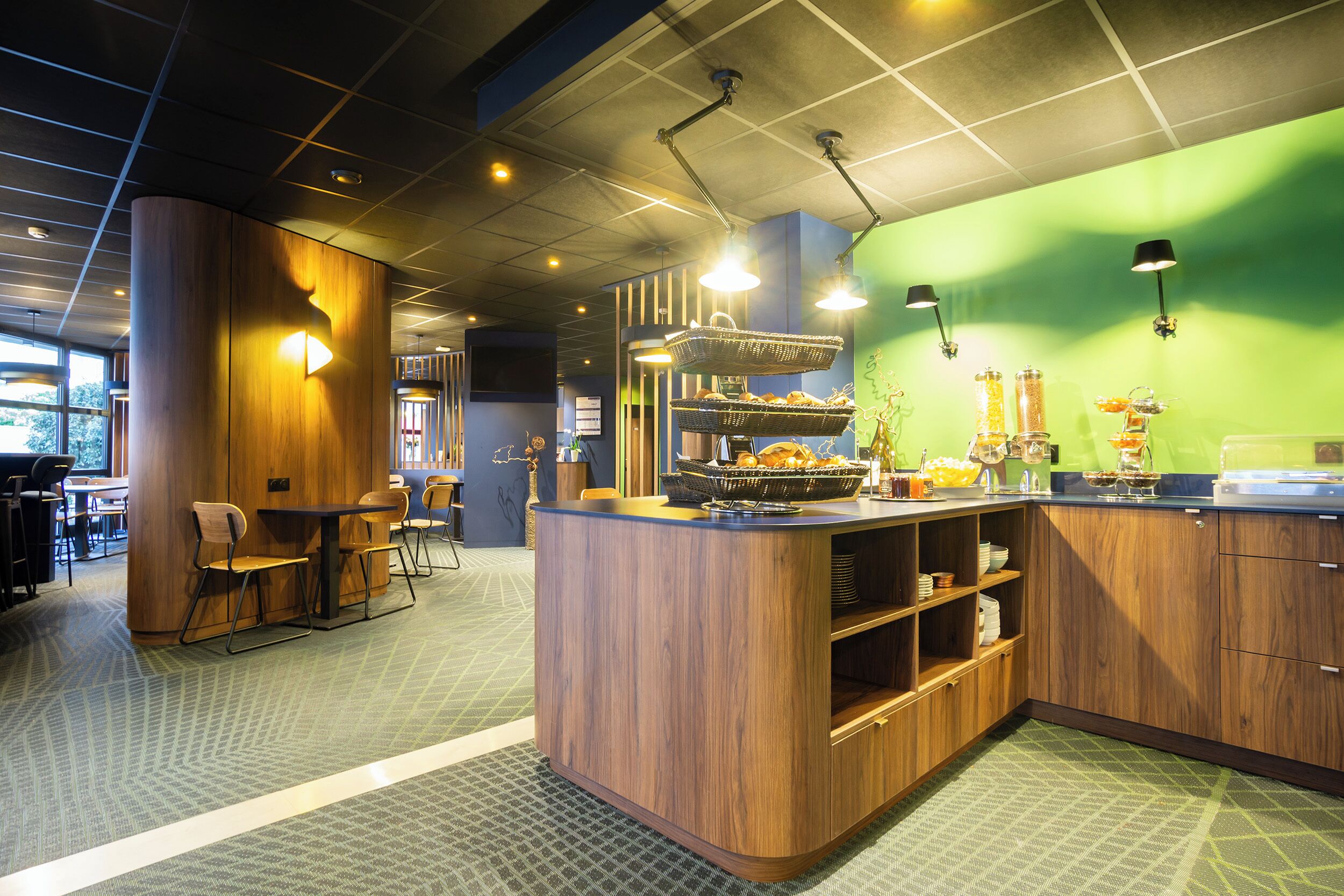 A modern kitchen area with wooden cabinets, a central island with seating, and a green accent wall.