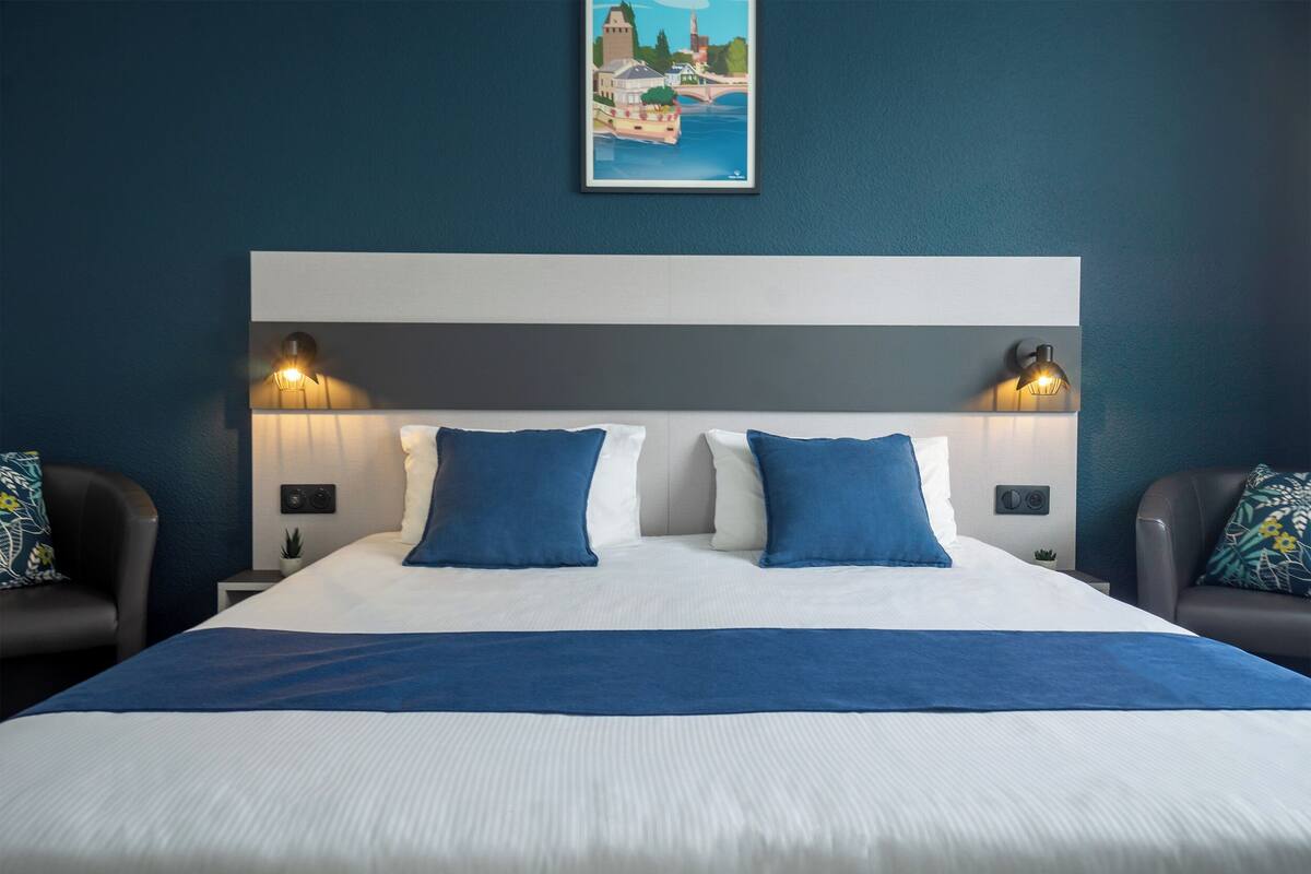 A hotel room with a large bed, two bedside lamps, a headboard, and a painting on the wall.
