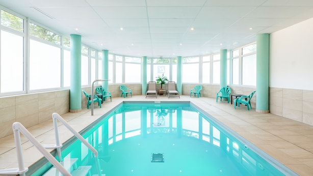 A large indoor swimming pool with clear blue water, surrounded by turquoise chairs and a sun terrace with a view of the trees outside. - Lagrange Apart'HOTEL Mulhouse (Mulhouse)