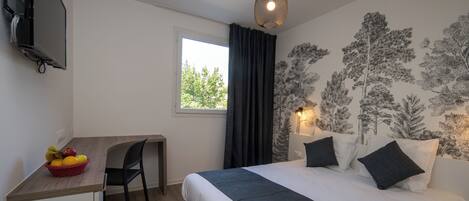 Ein Schlafzimmer mit einem Bett, einem Schreibtisch mit Obstkorb, einem Stuhl, einem Fenster und einer Wand mit einer Baummalerei.