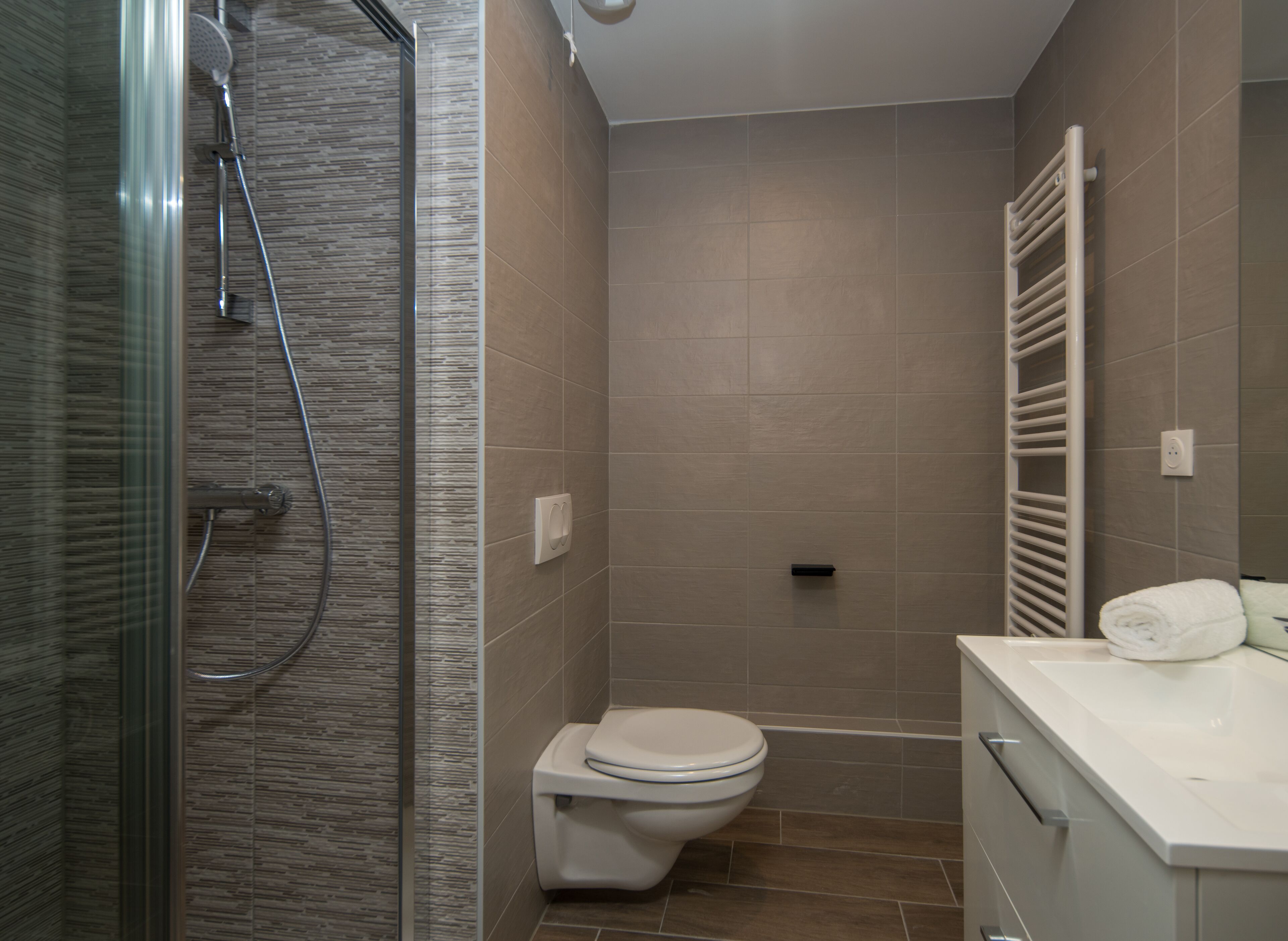 A modern bathroom with a glass shower enclosure, a toilet, and a white sink with a towel.
