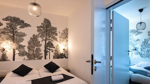 A modern hotel room with a large bed, two black pillows, a black throw blanket, and a wall mural of trees. - Lagrange Apart'HOTEL Mulhouse (Mulhouse)