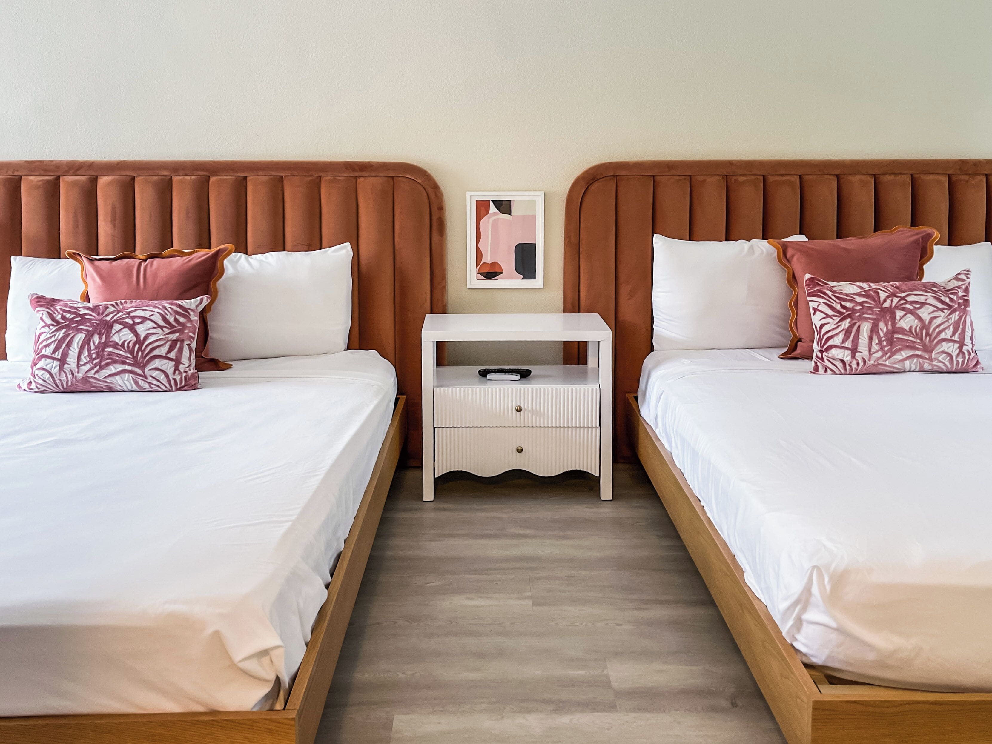 Une chambre avec un grand lit double, deux lits simples, une table de chevet et une œuvre d’art accrochée au mur.