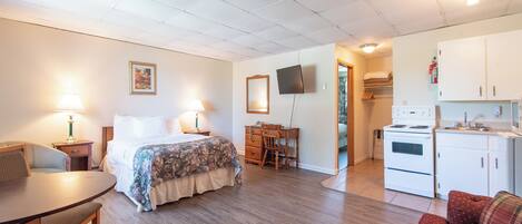 Una habitación de hotel compacta con cama, escritorio, kitchenette y zona de comedor.