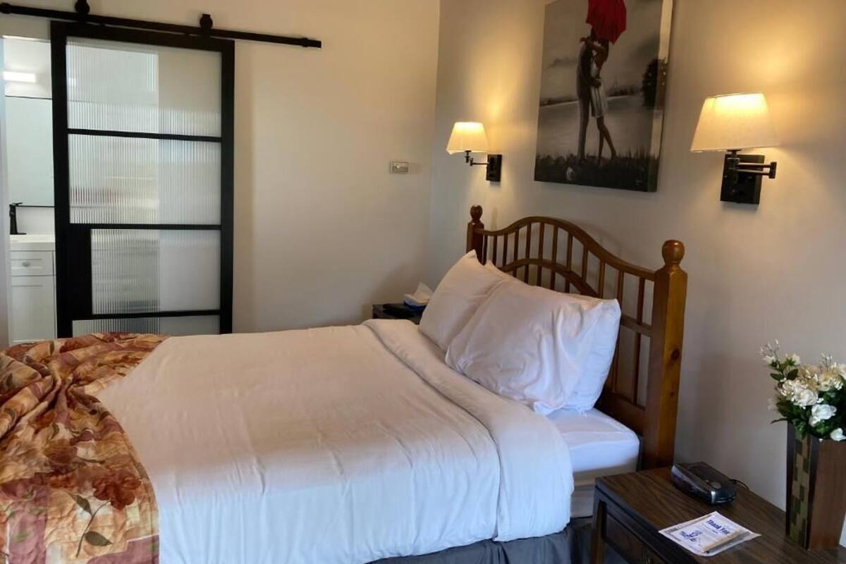 A hotel room with a bed, a nightstand, a lamp, a painting, and a sliding door.