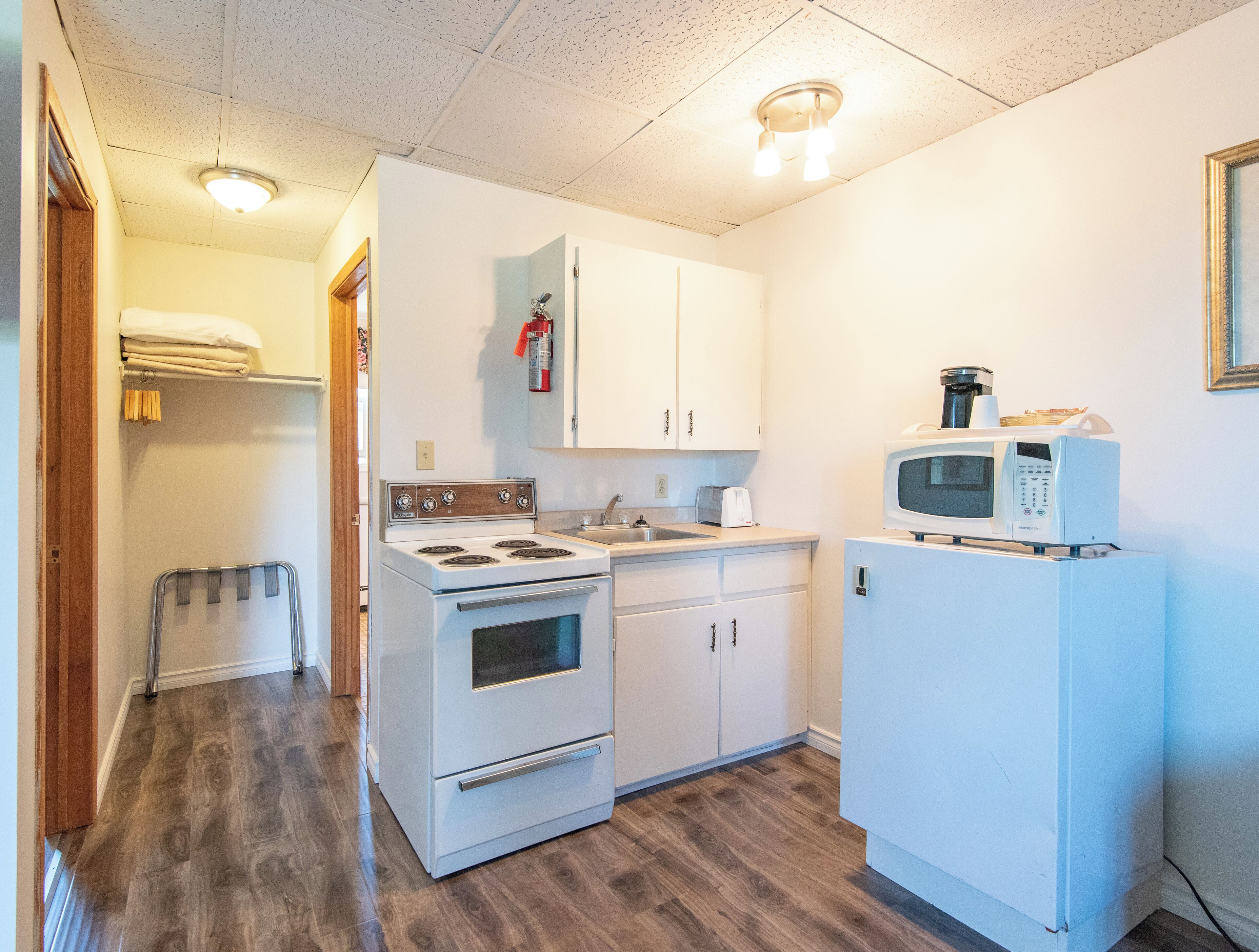 A compact kitchen with white cabinets, a stove, a sink, and a microwave.