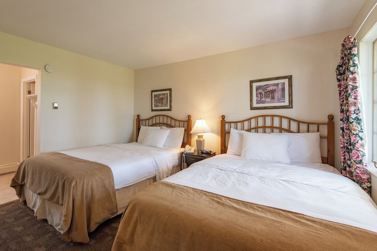 A hotel room with two single beds, a nightstand with a lamp, and a window with floral curtains.