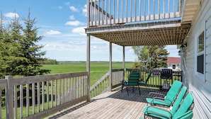 A wooden deck with green chairs, a barbecue grill, and a view of a green field and trees. - Canadas Best Value Inn & Suites Summerside (North Bedeque)