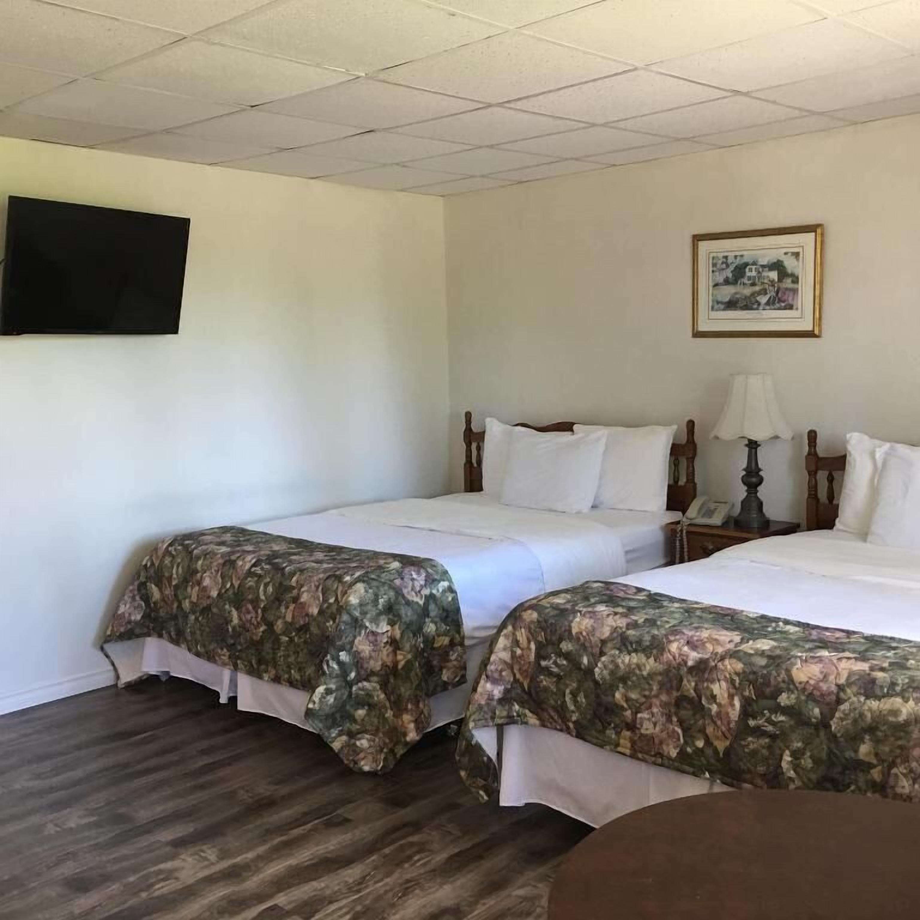 A hotel room with two beds, a flat-screen TV mounted on the wall, a framed picture, and a wooden floor.