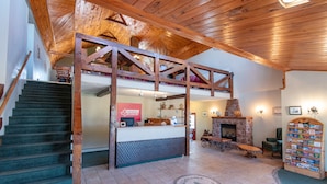 A spacious lobby with a wooden staircase, a reception desk, a fireplace, and a collection of books. - Canadas Best Value Inn & Suites Summerside (North Bedeque)