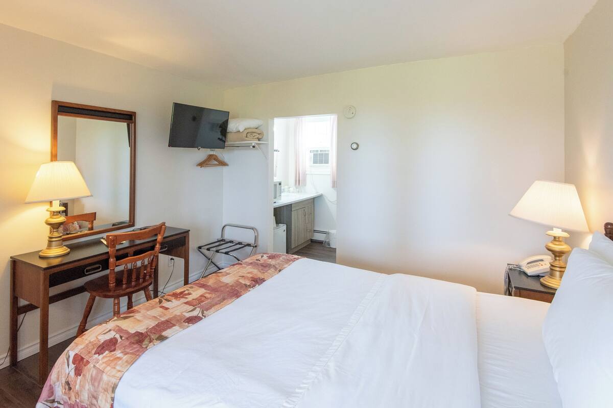 A hotel room with a bed, desk, chair, and a TV mounted on the wall.
