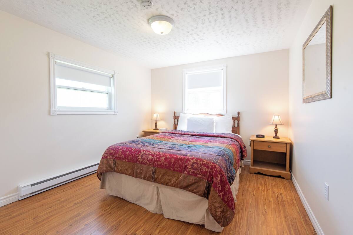 A bedroom with a bed, two bedside tables with lamps, a window, and a ceiling light fixture.