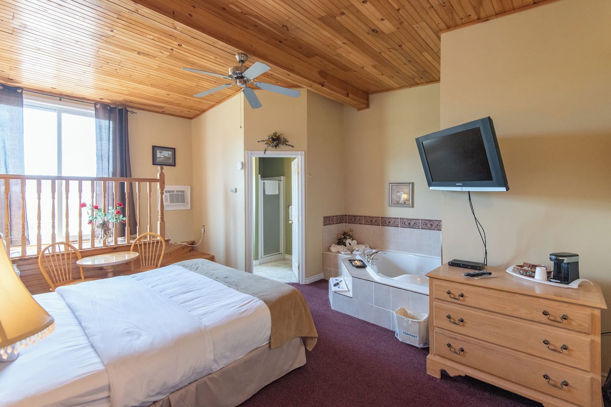 A hotel room with a bed, a desk, a chair, a TV, a dresser, and a bathroom.