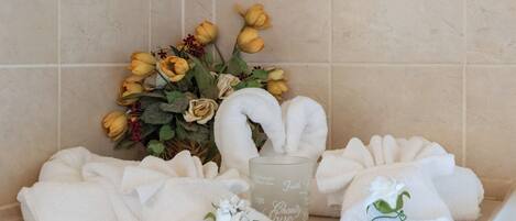 A bathroom with a towel rack holding several white towels, a glass candle with inscriptions, and a bouquet of yellow and white flowers.