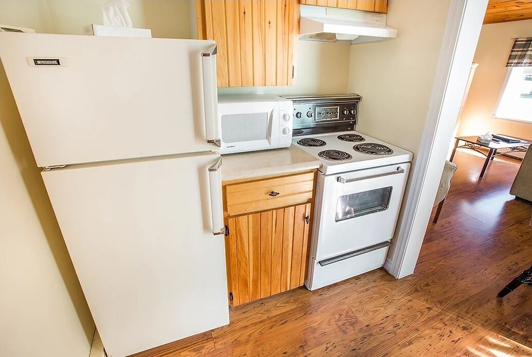 Cocina compacta con refrigerador, microondas, estufa y armarios de madera.