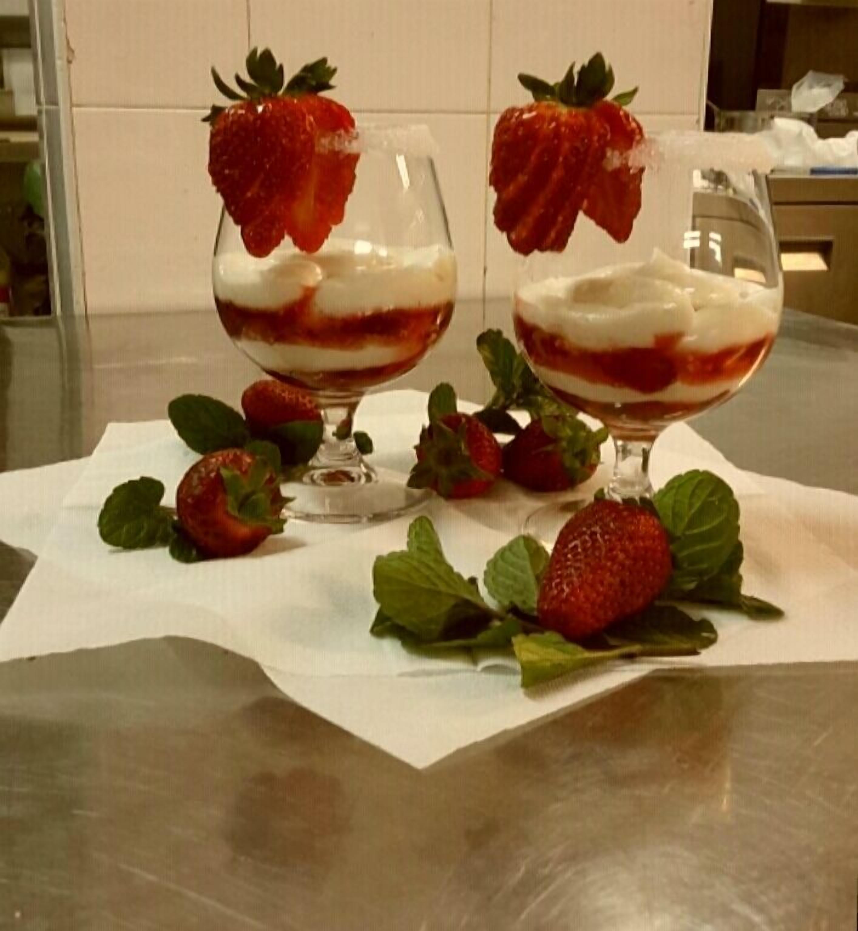 Dos vasos de postre con fresas encima, sobre una mesa con servilleta blanca.