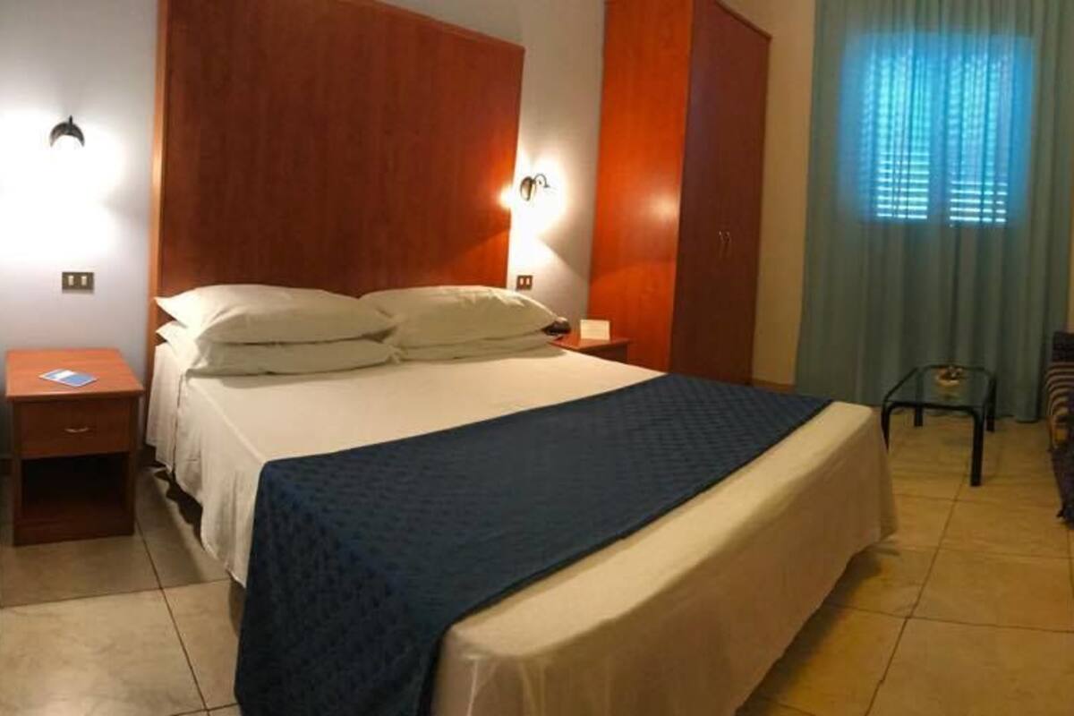 Una habitación de hotel con cama, escritorio, silla, televisión y espejo.
