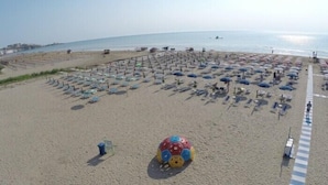 Une plage bordée de rangées de parasols et de chaises, un ballon de foot et une poubelle.