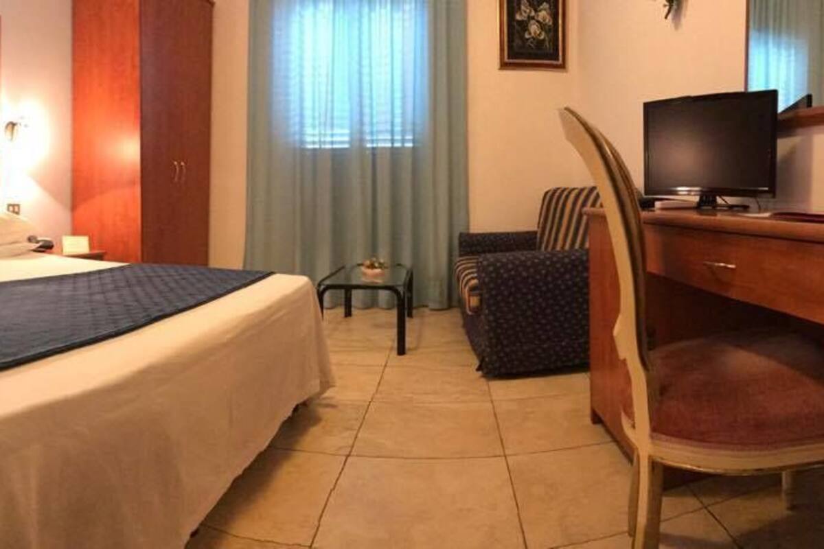 Una habitación de hotel con cama, mesita de noche, escritorio, silla y televisor.