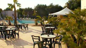 Un espace extérieur avec piscine, des chaises longues et des tables, entouré de palmiers et d’une tente blanche.