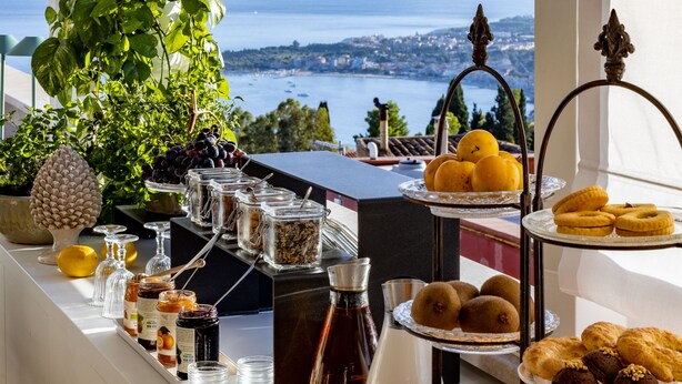 Una mesa de buffet con diversos alimentos y bebidas, con vistas a un paisaje pintoresco de agua y tierra a lo lejos.