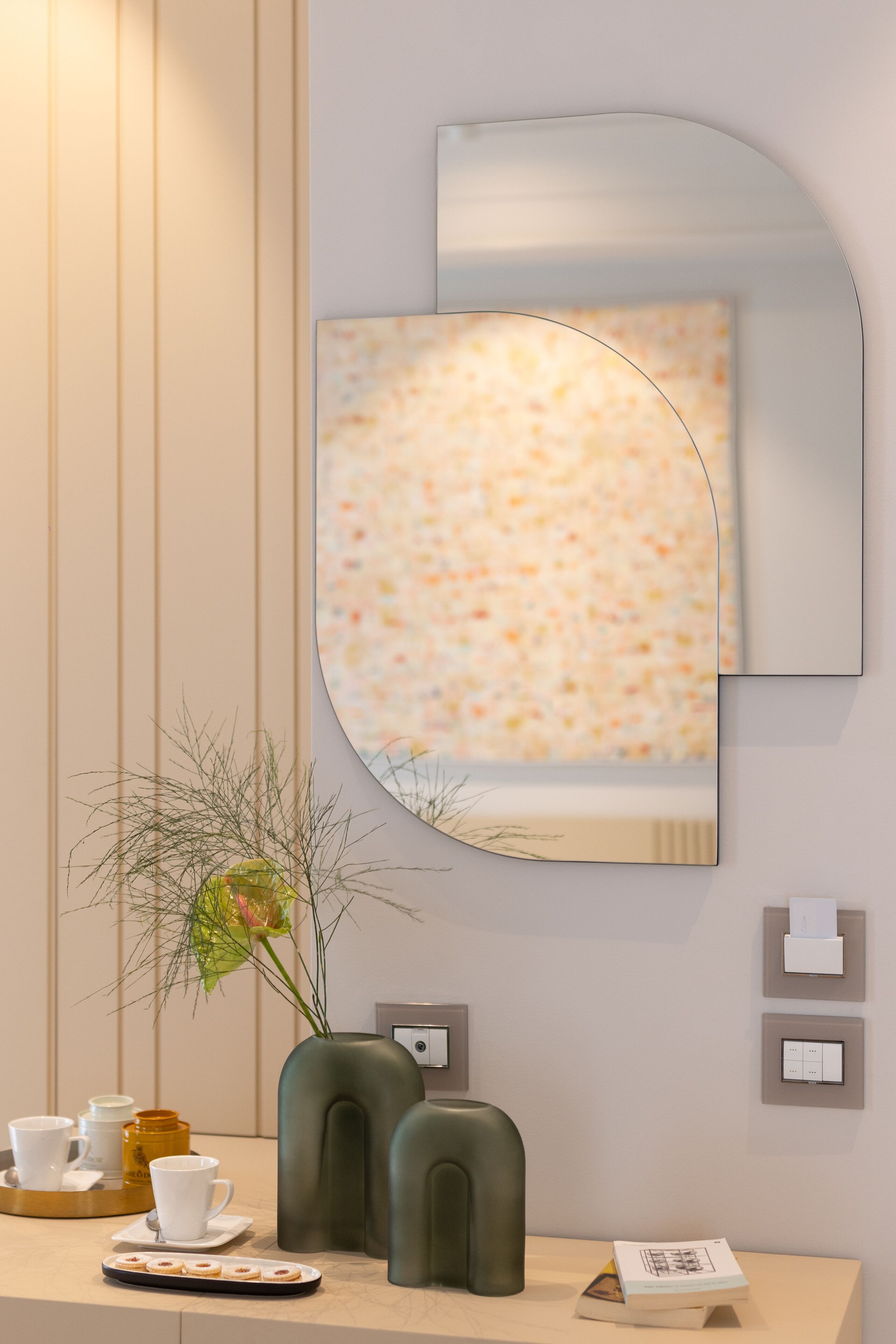 Une salle de bain moderne avec un grand miroir, un vase avec une plante et un plateau contenant des tasses et une théière.