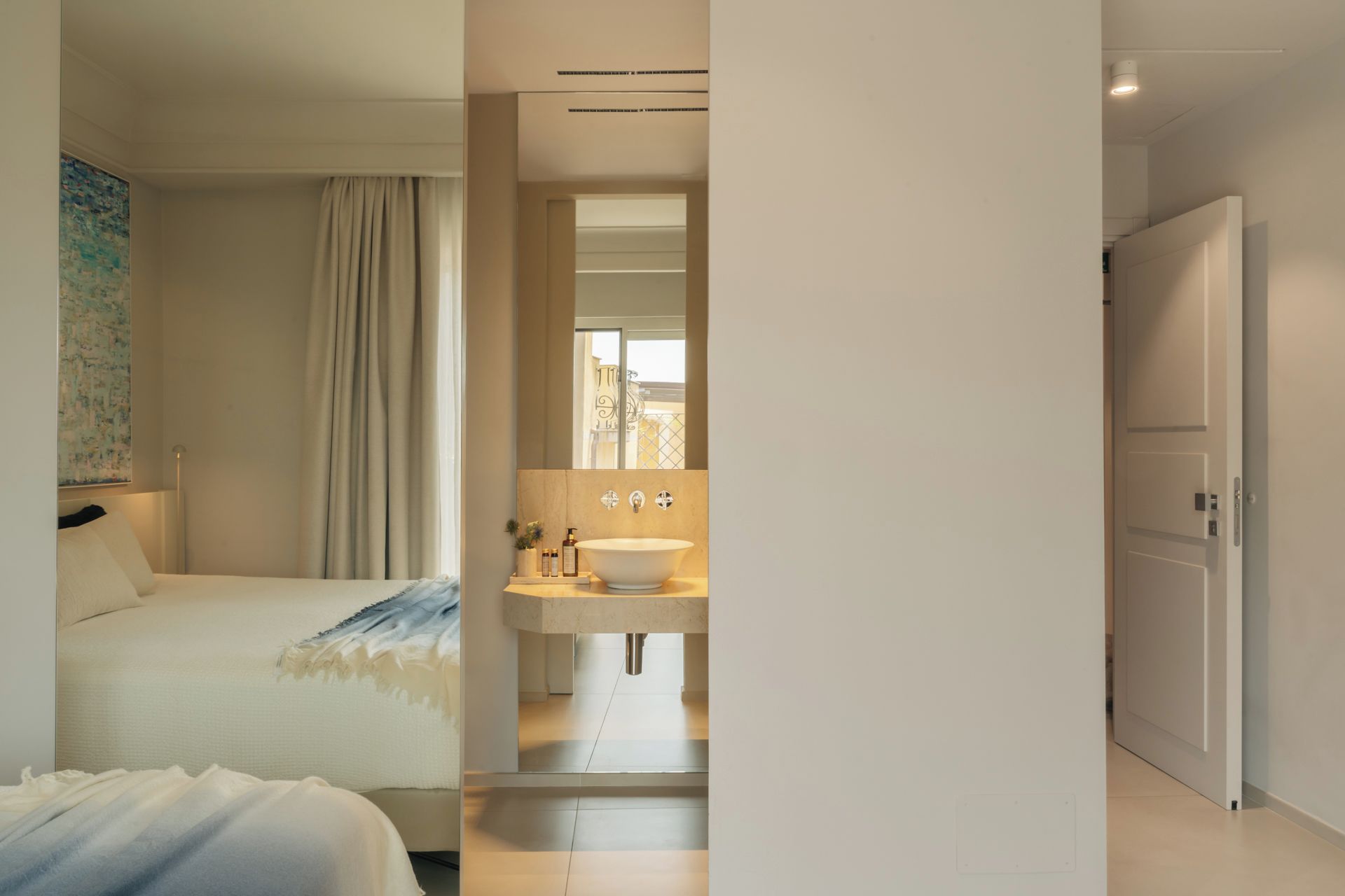 Ein Hotelzimmer mit einem Bett, einem Badezimmer mit Waschbecken und Spiegel sowie einer Tür zu einem weiteren Raum.