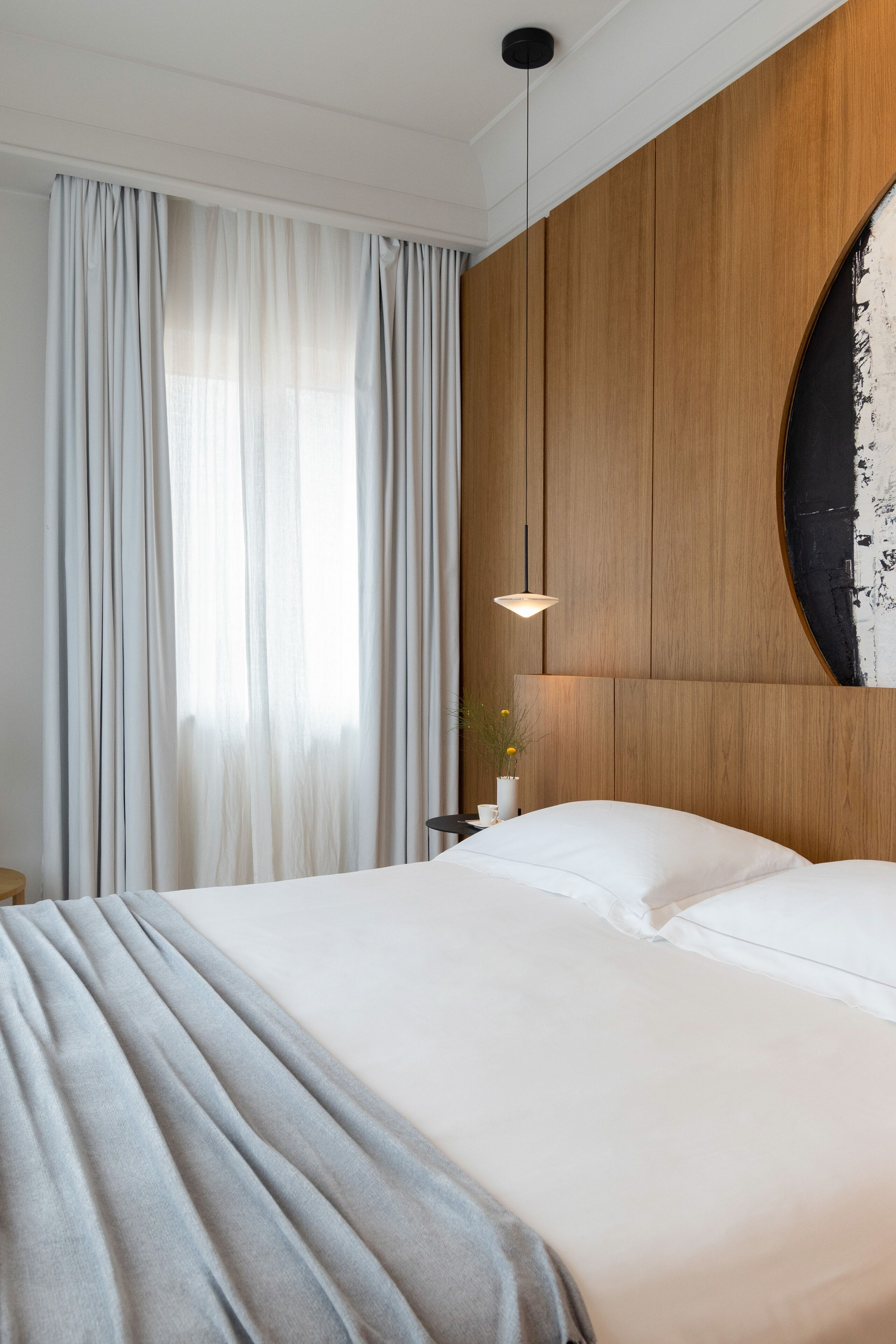 A hotel room with a large bed, a wooden headboard, and a hanging light fixture.
